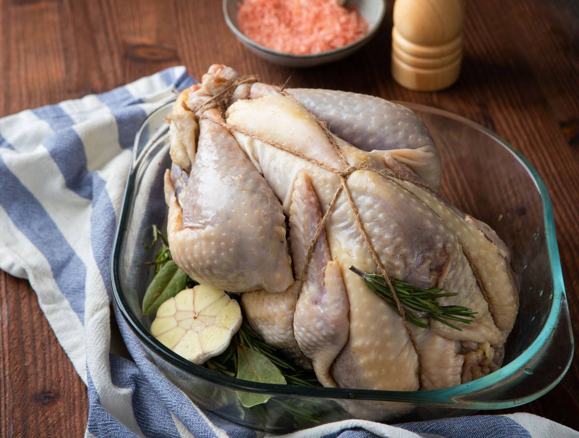 Rauw, opgebonden parelhoen in een glazen ovenschaal met knoflook en rozemarijn